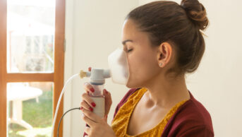 Young woman inhaling from nebuliser as part of cystic fibrosis treatment.