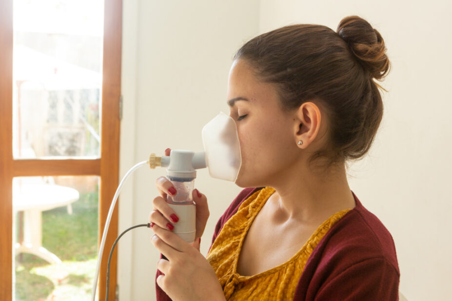 Young woman inhaling from nebuliser as part of cystic fibrosis treatment.