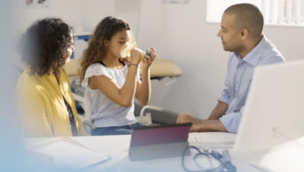 Photo of a male paediatrician teaching a young girl patient how to use inhaler in a doctor's office