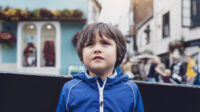 A worried child boy standing on a busy street in the centre of a city.