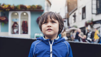 A worried child boy standing on a busy street in the centre of a city.