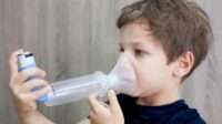 Young boy uses inhaler with spacer.