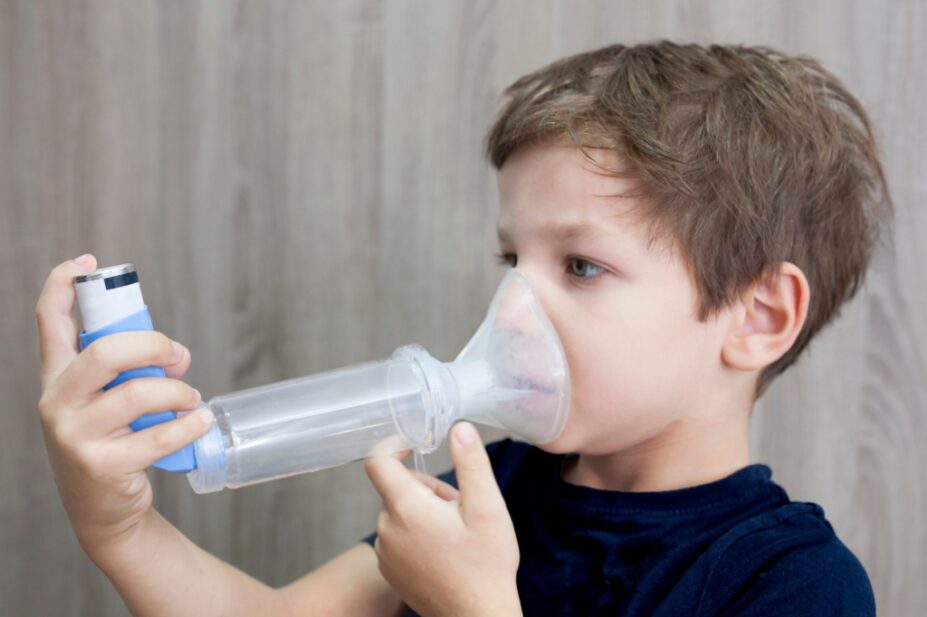 Young boy uses inhaler with spacer.