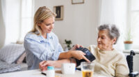 Photo of a female health professional measuring a blood pressure of a senior woman at home.