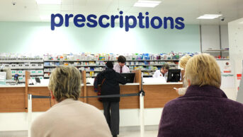 Community pharmacy counter with a queue of people waiting