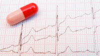 Photo of a pill resting on top of an ECG chart which shows escalating beats