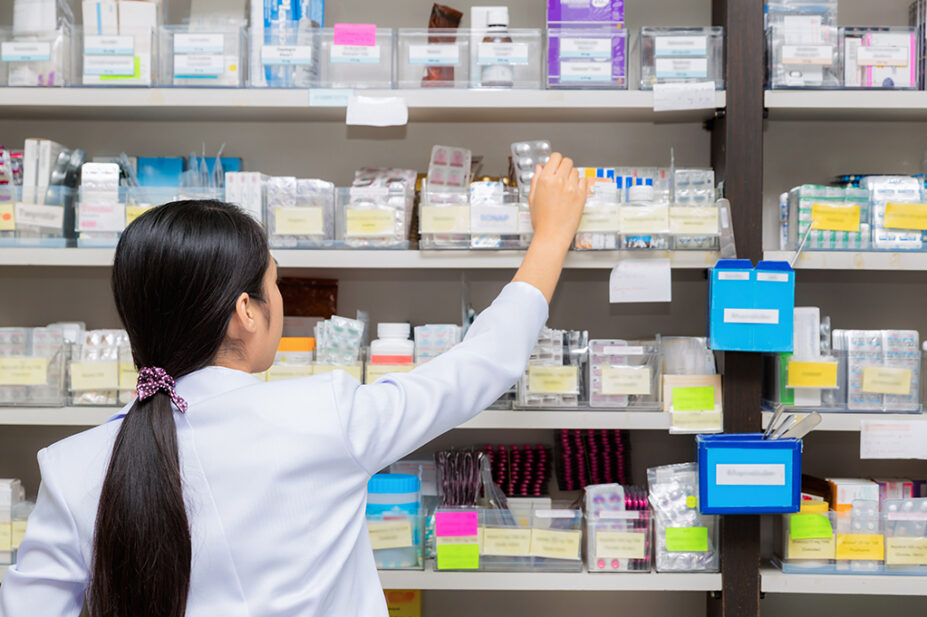 Asian pharmacist stocking shelves