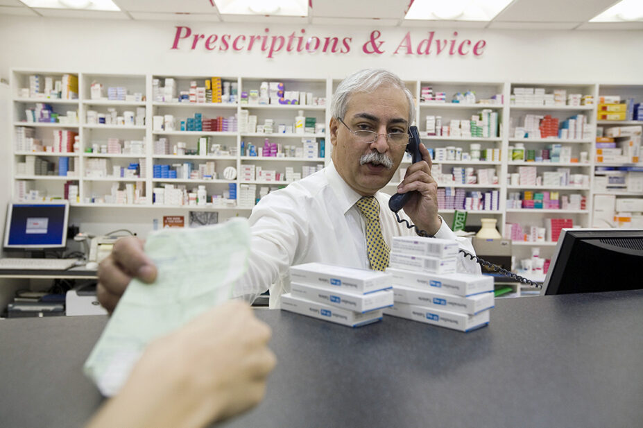 pharmacist taking someone's prescription from them while on phone