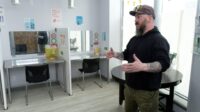 Photo of a tattooed manager of the safe injecting room explaining how it works in an interview in the space, which has cubicles, desks and needle disposal containers