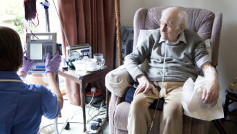 Nurse checking the infusion pump controlling a 94-year-old patient's blood transfusion in his home