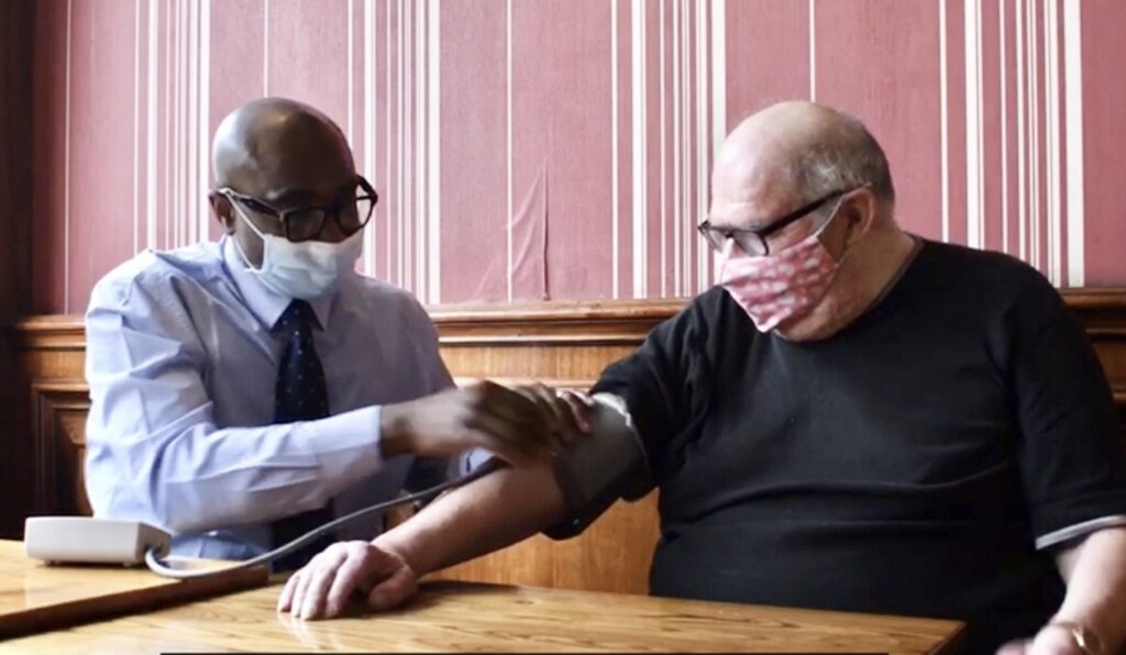 A pharmacist take an older man's blood pressure in a pub