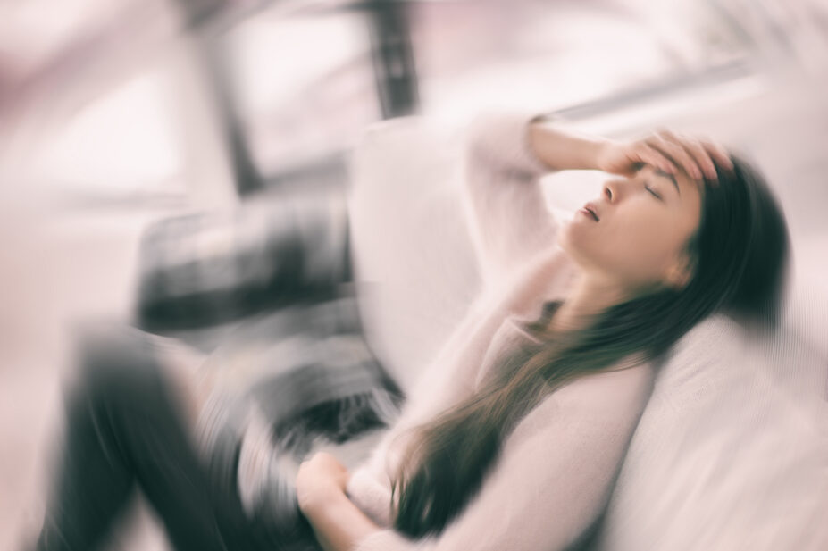 Sick woman with a headache/feeling faint and holding head in pain on a blurry motion blur background.