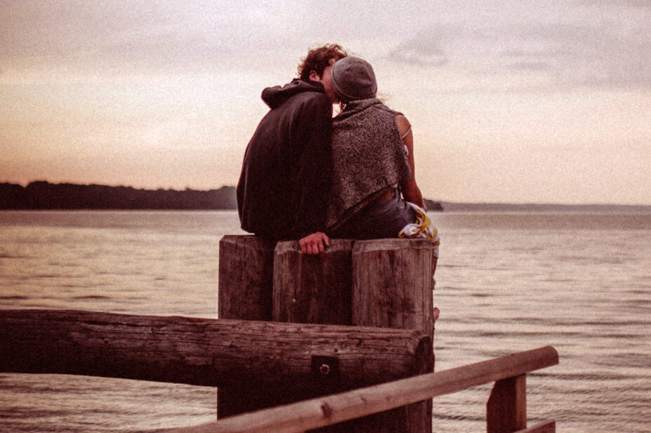 Photo of couple kissing on a pier at the sea