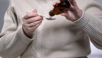 older woman taking medicine in syrup form