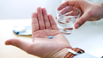 man's hands holding blue pill and glass of water