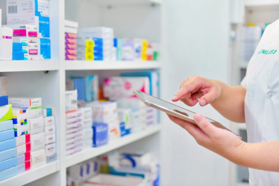 Photo of a pharmacist at shelves with an ipad to dispense medicines