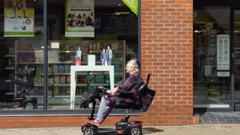 Photo of an older woman in a mobility scooter in front of a pharmacy