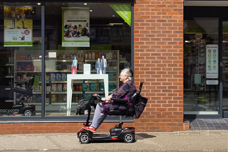Photo of an older woman in a mobility scooter in front of a pharmacy