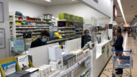 Photo of a customer at a Tesco Pharmacy waiting on a script, with two pharmacists in surgical masks behind the counter