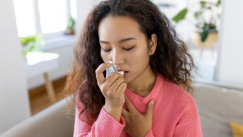 Photo of young Asian woman using inhaler while suffering from asthma at home