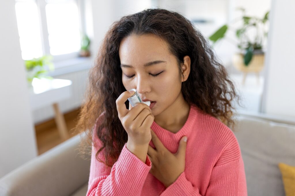 Photo of young Asian woman using inhaler while suffering from asthma at home