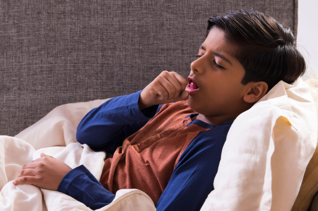 Young boy lying on the couch and coughing