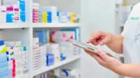 pharmacist holding digital tablet in front of medicines shelves