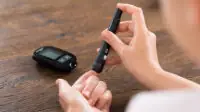 woman using finger prick test with glucose monitor on table