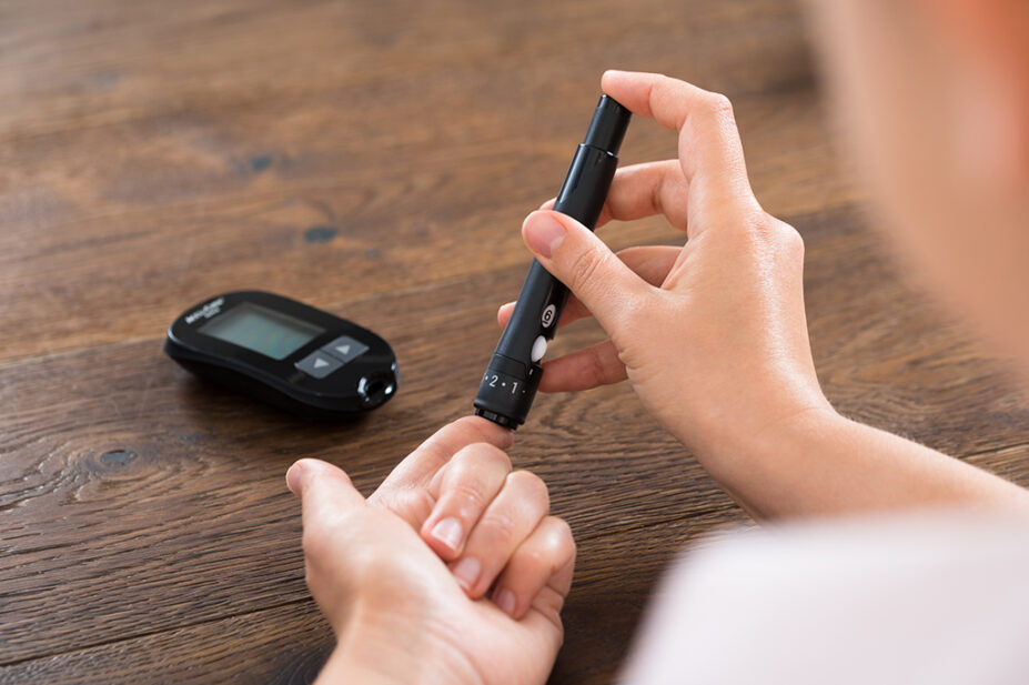 woman using finger prick test with glucose monitor on table