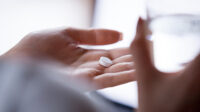 circular white pill in palm of woman's hand with glass of water in her other hand