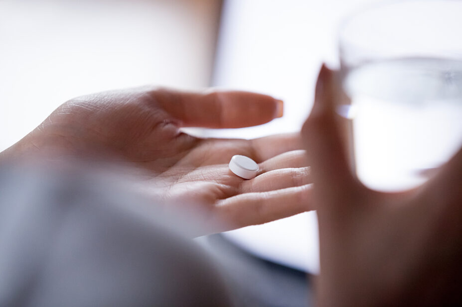circular white pill in palm of woman's hand with glass of water in her other hand