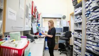 Pharmacist working at a computer in a pharmacy surrounded by medication shelves