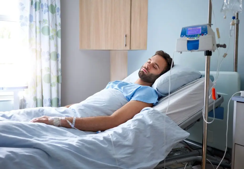 Sick young man attached to an intravenous drip lying on bed in a hospital room