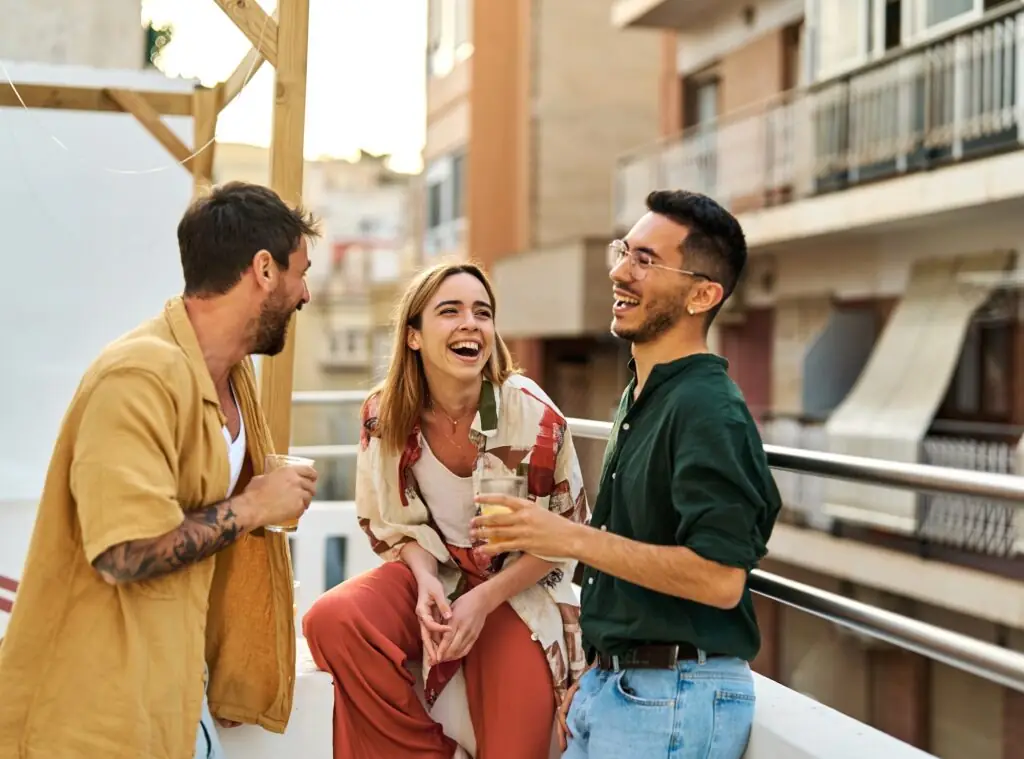 Happy young people having fun during a rooftop party during a summer holiday, standing on the rooftop terrace talking, eating and drinking