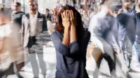 Crowd of people walking on a street in London in a blur, with a woman still, confused, in the middle