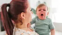 A mother holding a baby who is violently coughing