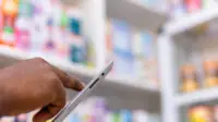 Close up of black person's hands in pharmacy, using a tablet, suggestive of medicine stock taking