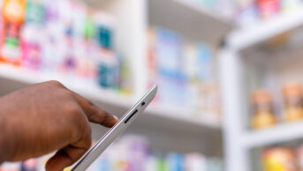 Close up of black person's hands in pharmacy, using a tablet, suggestive of medicine stock taking