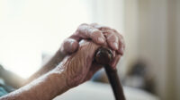 Older person's frail hands holding a walking stick