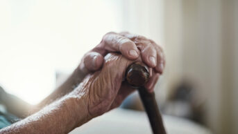 Older person's frail hands holding a walking stick