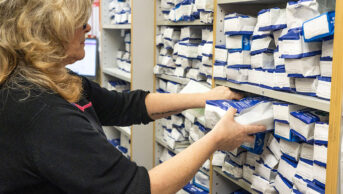 Pharmacy technician checking prescriptions on dispensary shelves