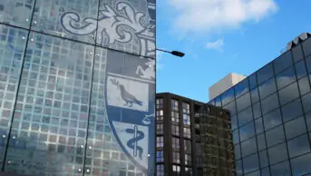 Photo of the outside of the Royal Pharmaceutical Society building on East Smithfield, with half of the RPS logo visible on a blue sky, and other buildings at angles in the background