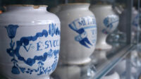 Photo of antique white medicine jars on a glass shelf in sharp perspective