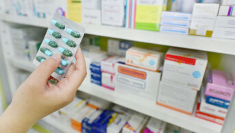 Packets of medicines in a dispensary, with hand holding blister pack of pills