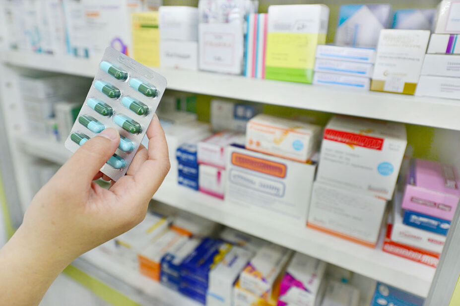 Packets of medicines in a dispensary, with hand holding blister pack of pills