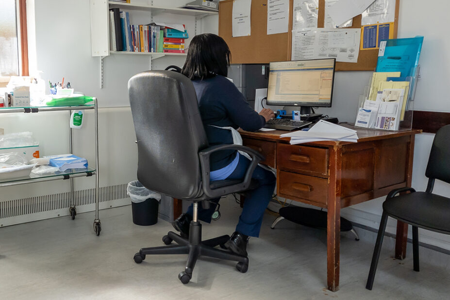 A GP working on a computer in consultation room