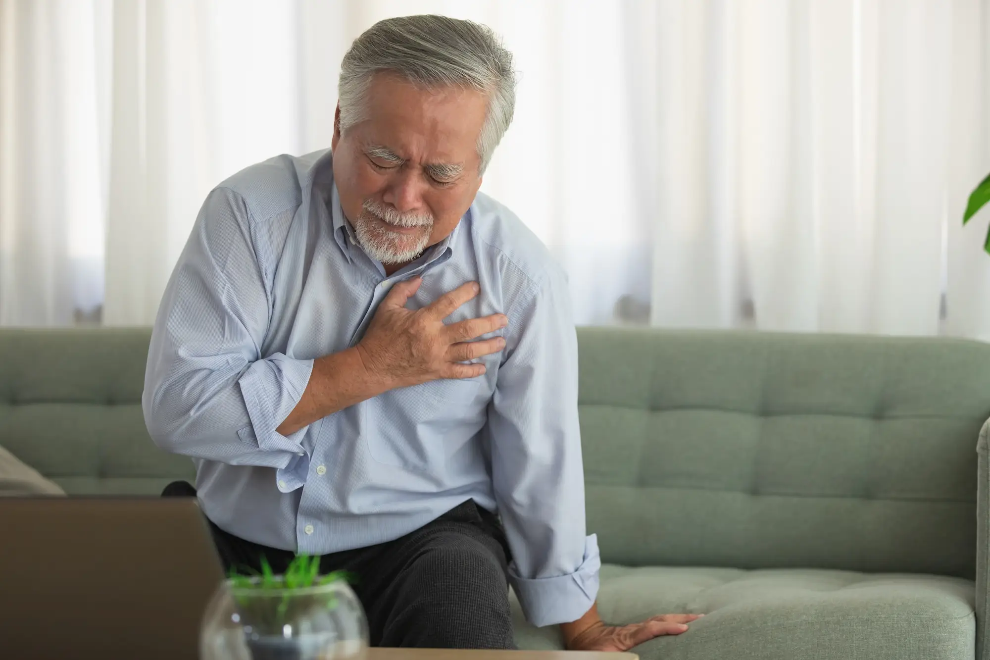 Photo of elderly Asian man clutching his chest in living room