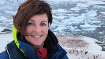 Photo of a woman smiling at the camera, with a sea of ice and penguins behind her