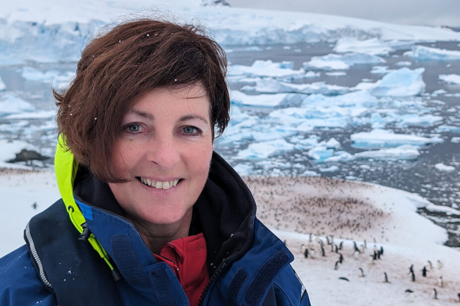 Photo of a woman smiling at the camera, with a sea of ice and penguins behind her