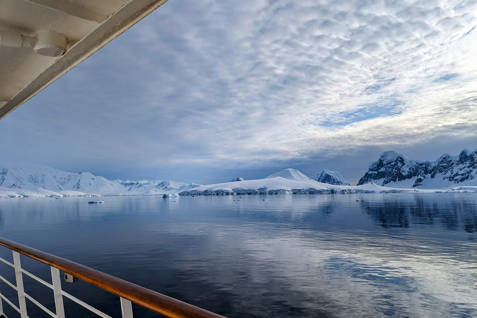 Photo of icebergs and an icy coast from the side of a boat, with the top of the rail and the boat awnings visible